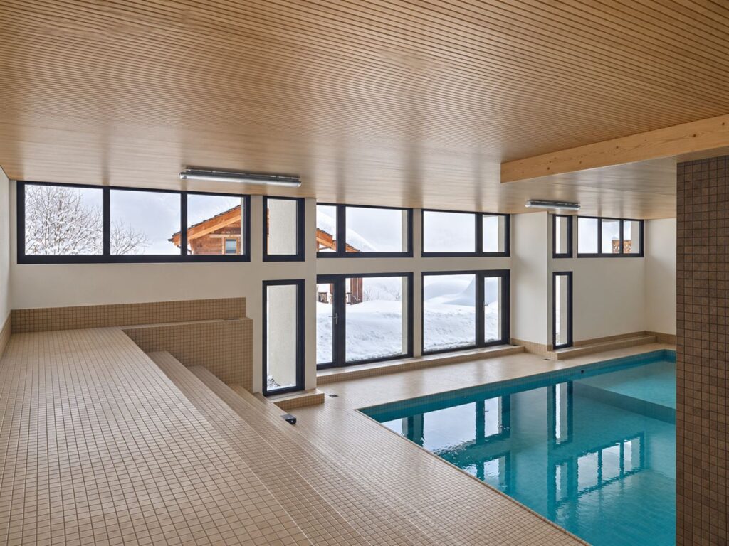 Piscine intérieure bordée de fenêtres et portes-fenêtres anthracite, vue sur la neige